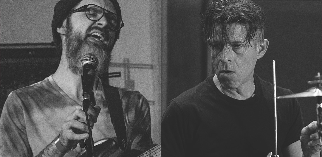 Two players in black and white, framed tight. One sings into the microphone, the other looks out from behind the drums beside a cymbal.